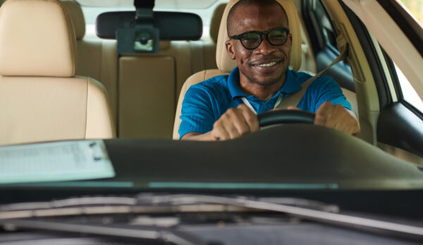 Happy but worried sweaty Black man driving car for the first time